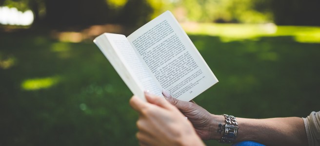 Someone sitting outside and reading a novel